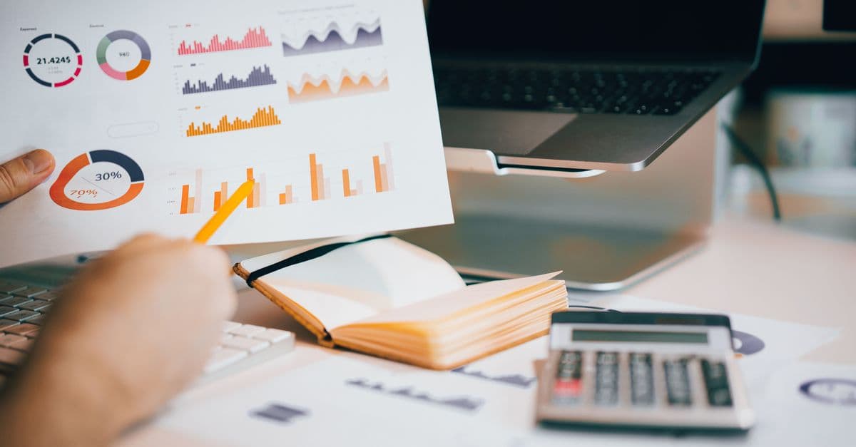 A hand holding a pencil over a sheet of financial graphs