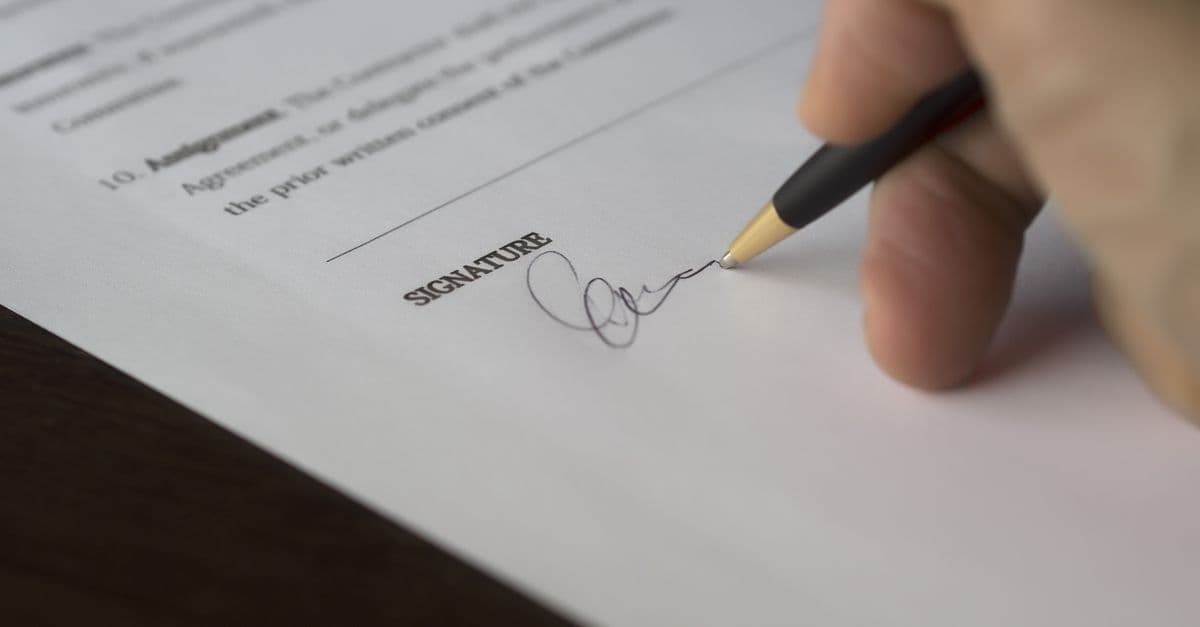 A hand signing a formal contract with a pen