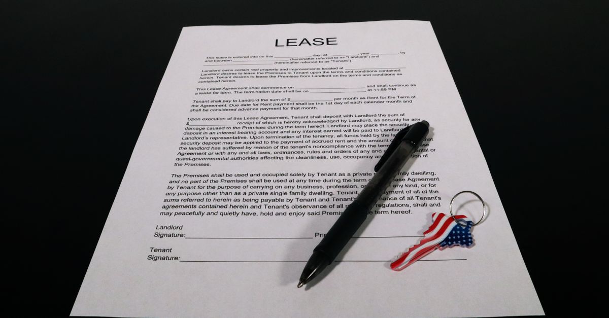 Two people shaking hands over a lease agreement on an office desk